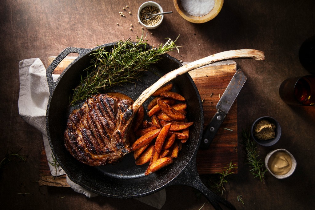 Grilled tomahawk steak in a cast iron skillet with crispy potato wedges and rosemary