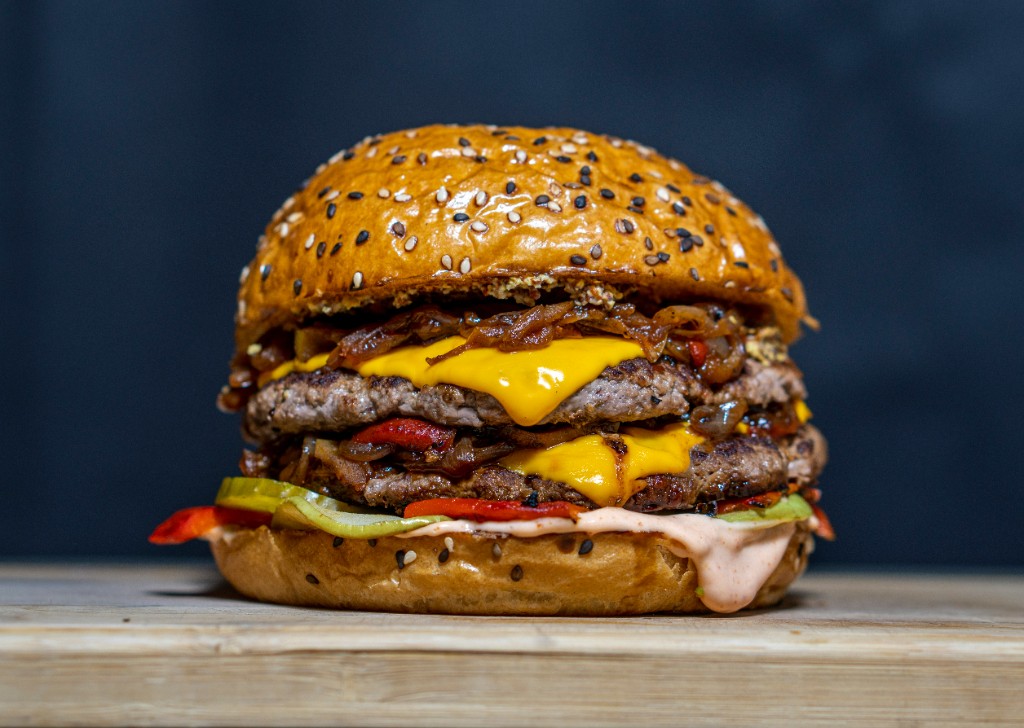 Tall double cheeseburger with melted cheese, caramelized onions, pickles, and sesame bun